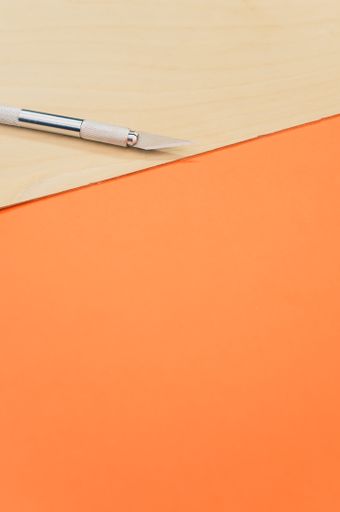 A vertical shot of the metallic scalpel on a plywood surface isolated on orange background