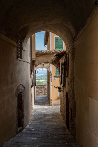 A vertical shot of a narrow road through the arches of the buildings in Tuscany, Italy