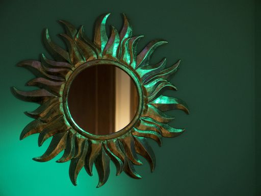 A round sun shaped mirror on a blue wall