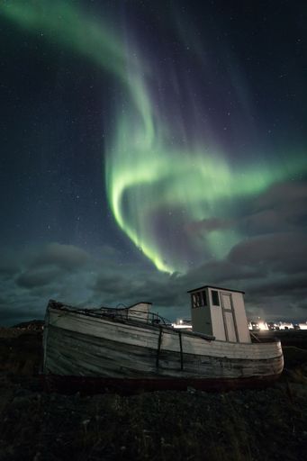 A vertical shot of the polar Aurora lights in a starry sky over a boat in a shote in Nordkapp, Norway