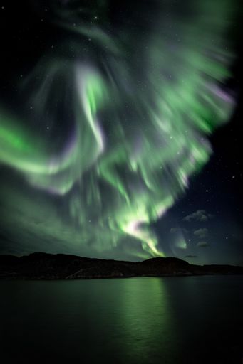 A vertical shot of the polar Aurora lights in the starry sky over the lake in Sor-Varanger, Norway