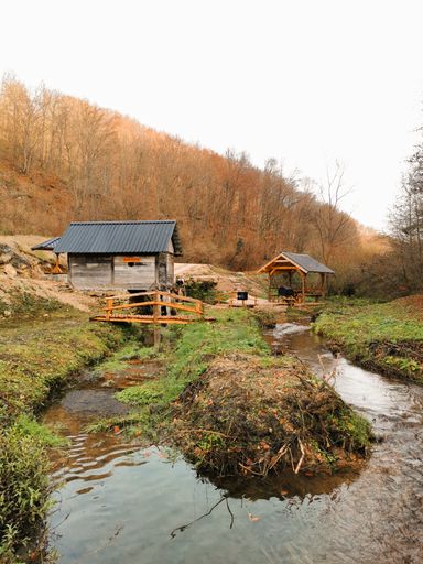 A vertical shot of wooden huts and a bridge over a narrow river in the autumn forest