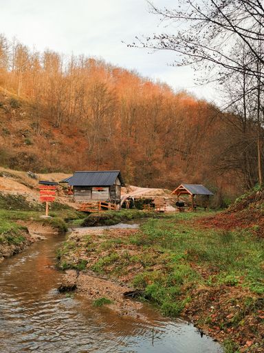A vertical shot of wooden huts and a bridge over a narrow river in the autumn forest