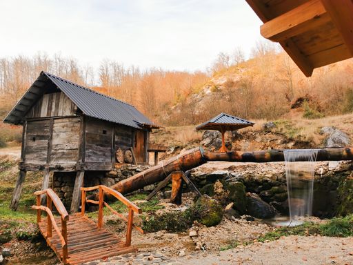 A closeup shot of a wooden hut and a bridge over a creek in the autumn forest
