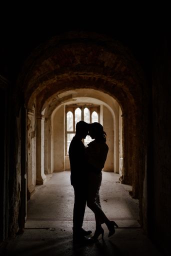 A vertical shot of a couple facing each other under an arch in an old building, silhouettes