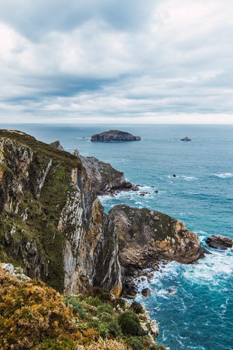 A vertical shot of the mountains near the sea under a cloudy sky in Cabo Penas, Asturias, Spain