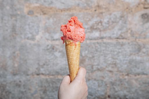 A closeup of a person holding strawberry-flavored ice cream with a cone under the lights