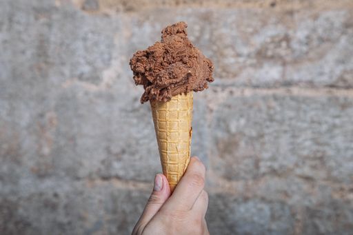 A closeup of a person holding chocolate ice cream with a cone under the lights