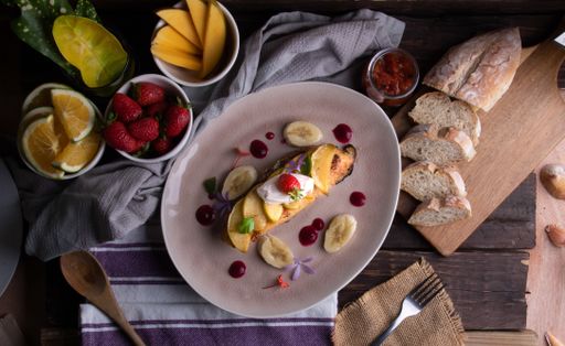 A meal of a steak with roasted apples, bananas, sauces, strawberries, mangos, oranges, sliced bread