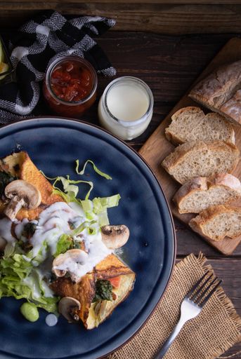 A serving of a delicious salad with greens, crepe with cheese, milk, mushrooms, bread, and fruits
