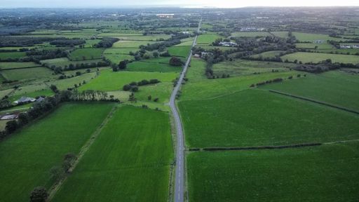 A bird's eye view of a highway in a green landscape of agricultural fields