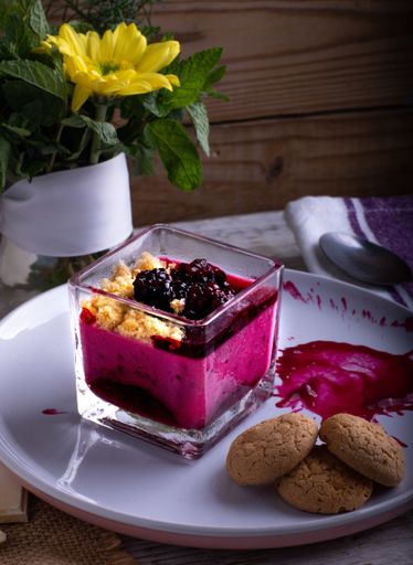 A vertical shot of blueberries on berries jam in a glass served with cookies on a plate