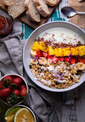 A vertical shot of healthy breakfast with oatmeal, pineapples, strawberries, bananas, bread, milk