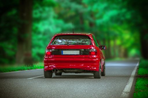 A low angle view of a red car riding on the road that goes through the forest on a blurry background