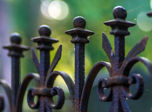 A low angle view of a rusty metallic fence with a spider web on it on a blurry background