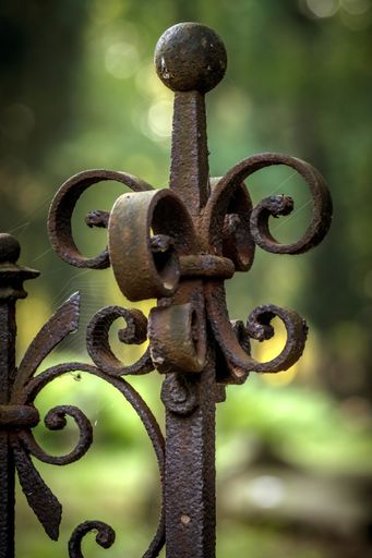 A low angle view of a rusty metallic fence with a spider web on it on a blurry background