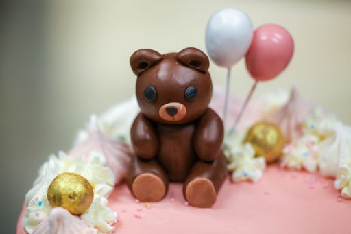 A closeup shot of a cute cake decorated with pink drips and a small bear with balloons on top