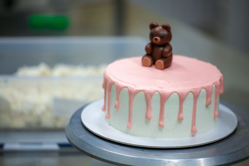 A closeup shot of a cute cake decorated with pink drips and a small bear on top