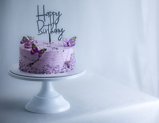 A frosted layered icing lilac cake with a happy birthday sign and butterflies