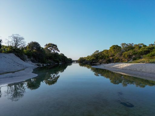 A reflecting river between trees with blue sky on a summer day
