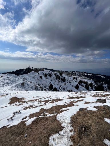 A vertical shot of white snow scattered on a mountain top under blue cloudy sky