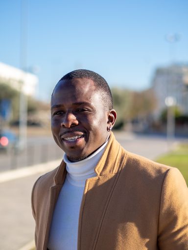 A shallow focus of an adult African male wearing a white turtleneck with a beige coat outdoors