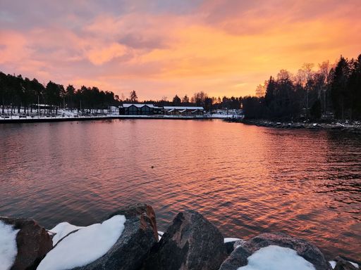A scenic landscape of a lake surrounded with forests and houses during a colorful sunset on a winter day