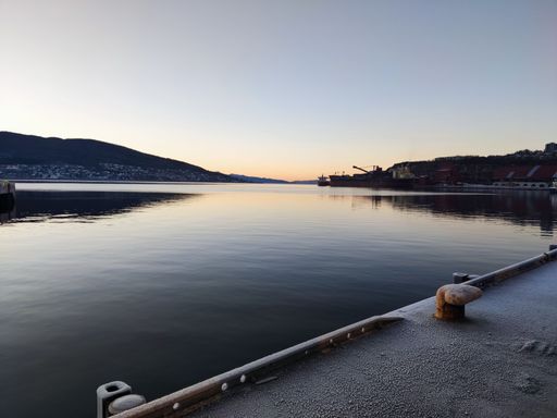 A scenic landscape of a lake surrounded with mountains and houses during sunset on a winter day