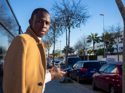 A shallow focus of a stylish African male leaning on a fence and texting on his phone