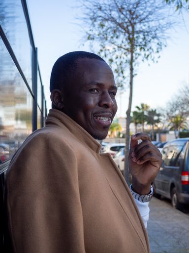 A shallow focus of a cheerful African male wearing a white turtleneck with a beige coat outdoors