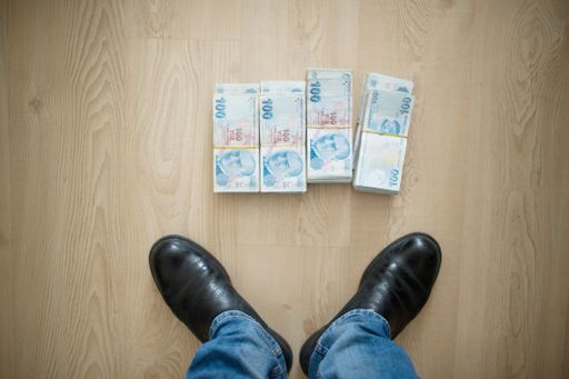 A high angle shot of a person standing next to stacks of money on a wooden surface