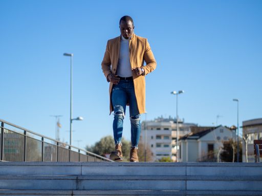 A shallow focus of an adult African male wearing jeans with a white turtleneck and beige coat and walking down the stairs