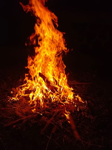 A vertical shot of a campfire outdoors at night with a dark blurry background