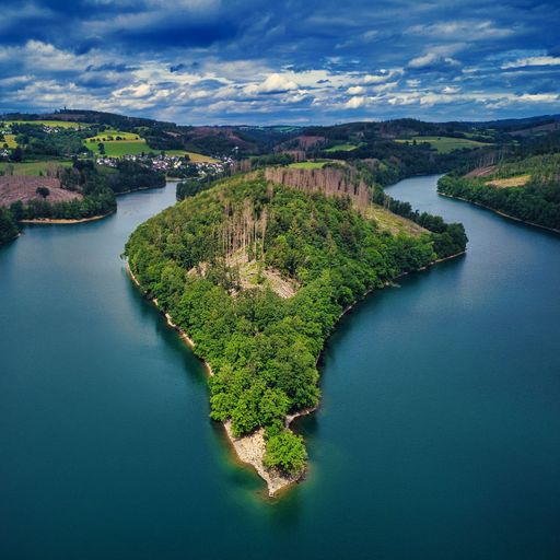 A drone view of hills and fields covered in greenery surrounded by the water on a cloudy day