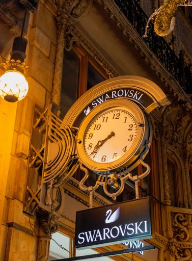 A low angle night shot of a clock the Swarovski jewelry logo in front of their store in Budapest
