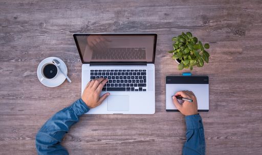 A top view of a man working on a laptop while drinking coffee