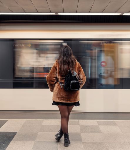 Rear view of woman standing on subway platform in front of moving train.