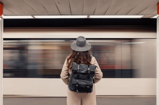 Rear view of woman standing on subway platform in front of moving train.