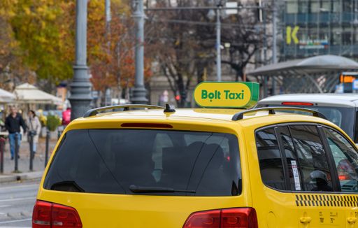 A closeup shot of a yellow car with a "Bolt Taxi" sign on a street in the city of Budapest