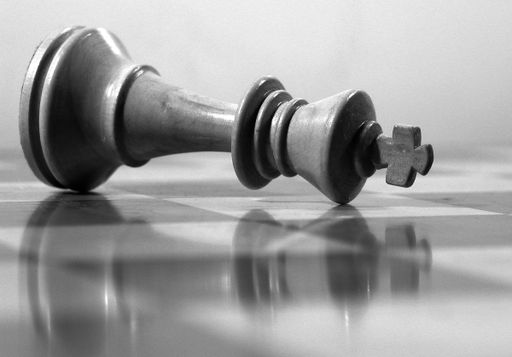 A grayscale shot of fallen black king figure and its reflection on the chessboard