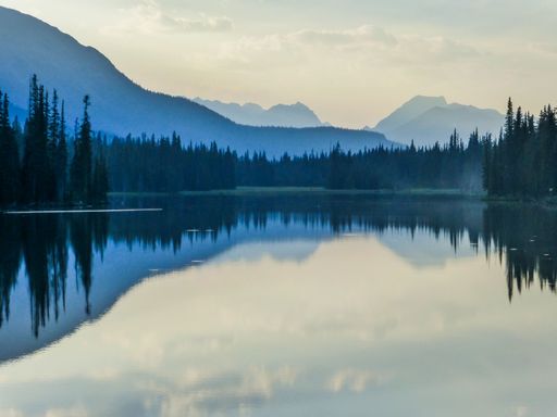 A beautiful view of a reflective lake surrounded by trees during sunrise