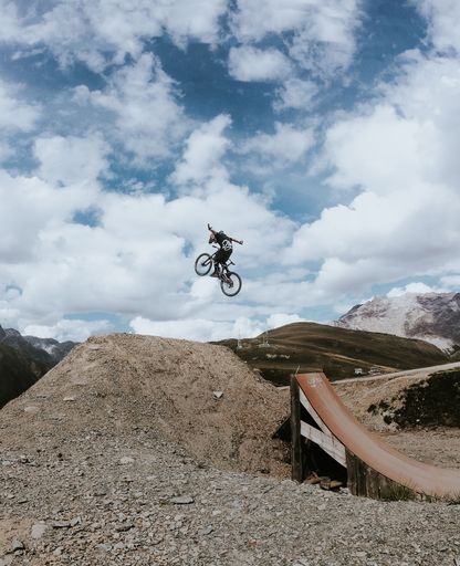 A vertical shot of a person doing tricks with their bike above a rocky hill