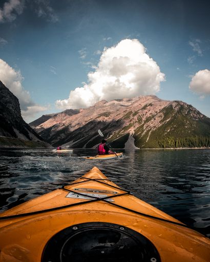 A vertical shot of people kayaking in a lake surrounded by rocky mountains