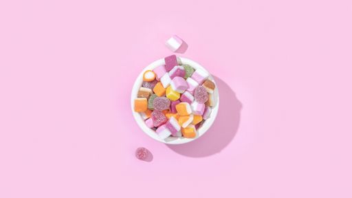 A top view of a bowl of jelly candies with different flavours isolated on a pastel pink background