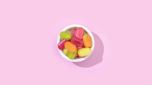 A top view of a bowl of jelly candies with different flavours isolated on a pastel pink background