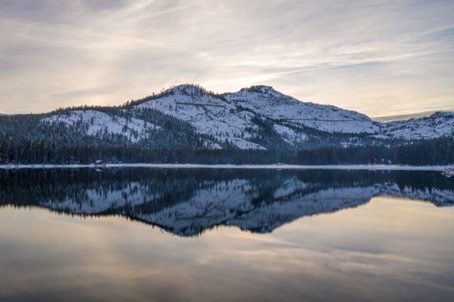 A snow-covered mountain and cloudy sky reflects beautifully on the tranquil surface of an alpine lake.