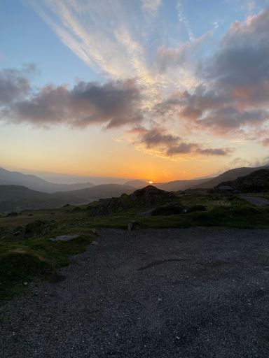 A vertical shot of a cloudy sunset sky over silhouetted mountains