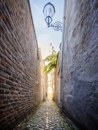 A vertical of a narrow alley, walkway between a building with red brick and another with rough surface