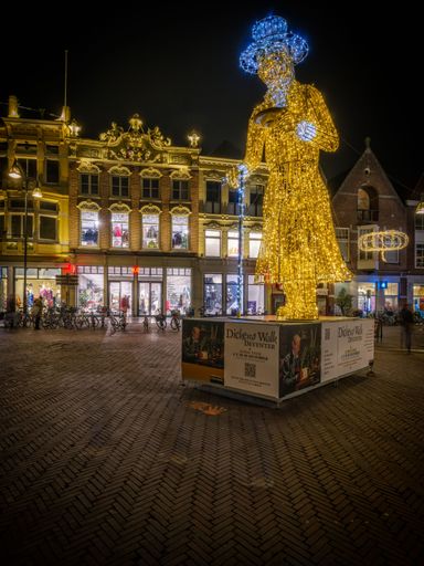 A vertical shot of the Scrooge light object on the main square of Deventer city at night with buildings and bikes in the background in Netherlands