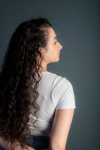 Profile of beautiful young woman with black hair wearing white shirt. Against gray background. 